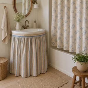 Sky blue stripe viscose linen blend sink skirt installed around a bathroom pedestal sink, adding stylish concealed storage with a fresh cottage-inspired look.