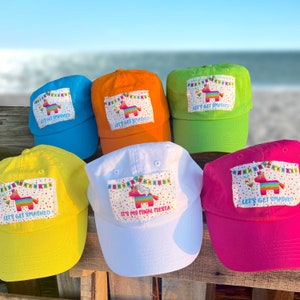 May include: Six colorful baseball caps with different designs featuring a pinata and the text "Let's Get Smashed" or "It's My Final Fiesta".