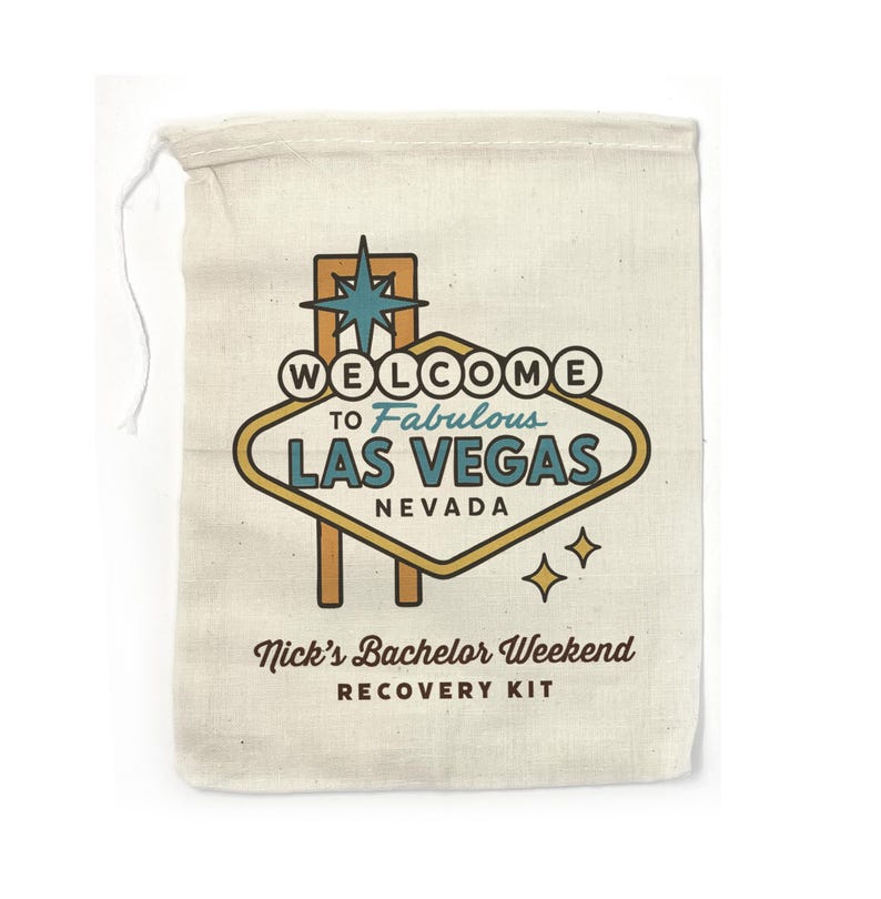May include: A white canvas bag with a drawstring closure. The bag features a retro-style illustration of the Las Vegas sign with the text "Welcome to Fabulous Las Vegas, Nevada". Below the sign, the text reads "Nick's Bachelor Weekend Recovery Kit".