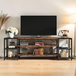 Puede incluir: Un televisor negro se encuentra sobre un mueble de TV con múltiples estantes. El mueble tiene un marco de metal negro y estantes de madera envejecida. Libros, esculturas y un teléfono vintage adornan los estantes, creando un centro de entretenimiento elegante.