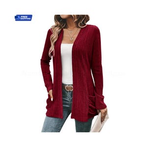 May include: A burgundy ribbed knit cardigan with long sleeves and front pockets. The open-front design features a V-neckline. The model is wearing a white top and blue jeans. A gold-tone belt with a circular buckle is visible.
