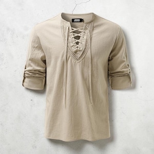 May include: Beige linen shirt with a lace-up neckline and rolled-up sleeves. The shirt has a V-neck design with intricate detailing around the neckline. The sleeves are three-quarter length, and the fabric appears to be lightweight and breathable.