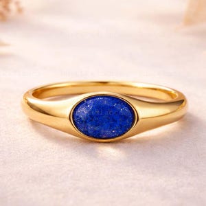 May include: A gold ring with a vibrant blue oval gemstone. The ring has a smooth, polished band and a bezel setting that securely holds the gemstone. The ring is a piece of jewelry.
