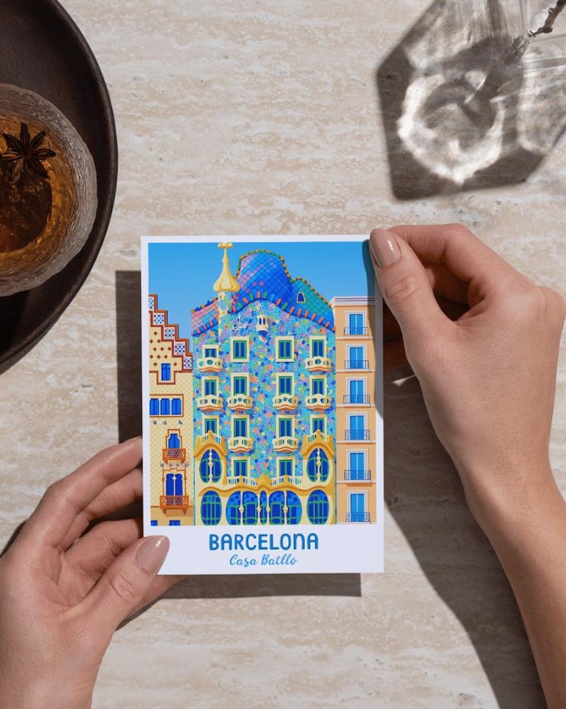 May include: A postcard featuring a colorful illustration of Casa Batll&oacute; in Barcelona. The building has a blue, mosaic-tiled roof and ornate facade with arched windows. The text "BARCELONA Casa Batll&oacute;" is printed at the bottom against a blue sky background.