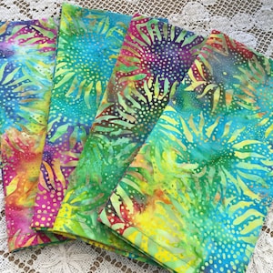 May include: Four colorful fabric napkins with a batik design featuring a swirling pattern of green, blue, yellow, and pink.