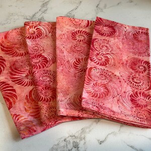 May include: Set of four red and orange fabric napkins with a spiral pattern. The napkins are made of cotton and are perfect for everyday use.