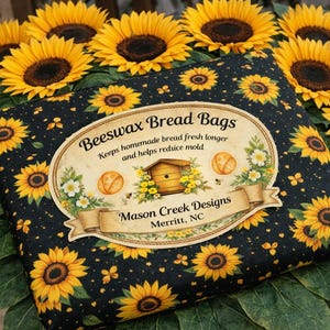 May include: Black beeswax bread bag with a sunflower pattern. The bag has a label that reads "Beeswax Bread Bags" and "Mason Creek Designs, Merritt, NC". The bag is surrounded by sunflowers.