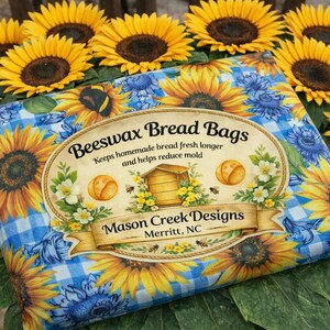 May include: A blue and yellow Beeswax Bread Bag with a sunflower and gingham pattern. The bag is surrounded by sunflowers. The label reads "Beeswax Bread Bags" and "Mason Creek Designs, Merritt, NC."
