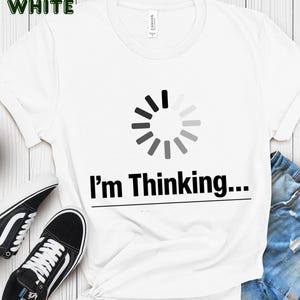 May include: White t-shirt with the text "I'm Thinking..." below a loading symbol graphic. The shirt is paired with black and white sneakers and blue jeans. The word "WHITE" is in green in the top left corner.