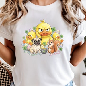 May include: White t-shirt featuring a cartoon illustration with an angry yellow duck, three smaller ducks, a pug, and a squirrel. The design includes Easter eggs, shamrocks, and a pot of gold.