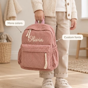 Pode incluir: Uma mochila de veludo cotelê rosa empoeirado com bolso frontal com zíper, bolsos laterais e alça superior. O nome Olivia está bordado em branco na frente. Duas caixas de texto estão visíveis com os rótulos More colors e Custom fonts.