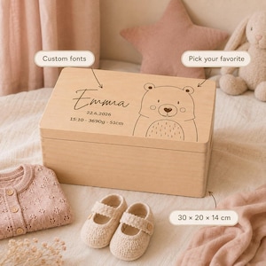 Pode incluir: Uma caixa de recordações retangular de madeira com uma ilustração de urso gravada a laser, o nome Emma, data 22.6.2026, 15:10, 3690g e 51cm. Etiquetas de texto indicam fontes personalizadas e dimensões de 30 x 20 x 14 cm.