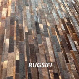 Könnte beinhalten: Ein rechteckiger Teppich mit Patchwork-Design. Der Teppich besteht aus rechteckigen Teilen in Braun-, Grau- und Beigetönen. Das Wort "RUGSIFI" ist weiß auf dem Teppich aufgedruckt.