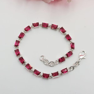 Op de afbeelding: Een zilveren armband met rechthoekige, robijnrode edelstenen. De edelstenen zijn gezet in een zilveren ketting en de armband heeft een karabijnsluiting. De armband wordt gepresenteerd op een witte ondergrond.