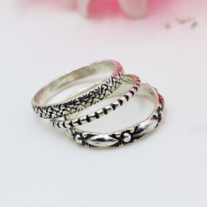May include: Three silver rings with detailed patterns. One ring has a floral design, another has a series of dashes, and the third features a leaf and dot motif. The rings are stacked, creating a layered effect.
