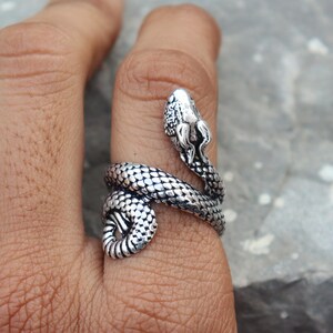 Peut inclure: Une bague argentée en forme de serpent enroulée autour d'un doigt. La bague présente une tête et un corps de serpent détaillés avec des écailles texturées. La tête du serpent est relevée.