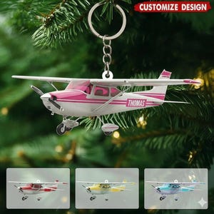 May include: A personalized airplane keychain with a pink and white design, the name "Thomas" is printed on the side. The keychain hangs from a silver ring and chain. Additional airplane keychains in red, yellow, and blue are shown below.