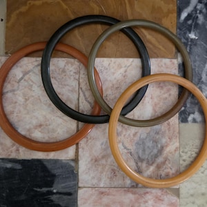 May include: Four interlocking, circular, wooden handbag handles in shades of brown, black, and tan. The handles are arranged in a pattern against a background of marble tiles. The handles are approximately 6 inches in diameter.