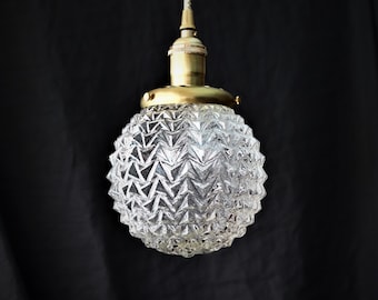 May include: A gold pendant light with a clear glass shade that has a textured pineapple design.