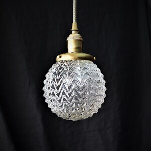 Op de afbeelding: Een gouden hanglamp met een heldere glazen kap met een getextureerd ananasontwerp.
