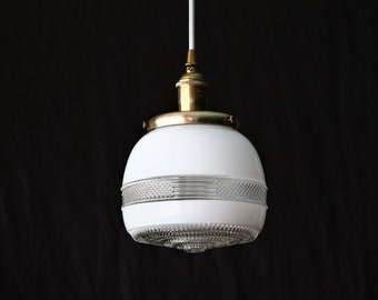 May include: A white glass pendant light fixture with a brass finish and a clear glass diffuser. The light fixture has a geometric pattern on the glass.