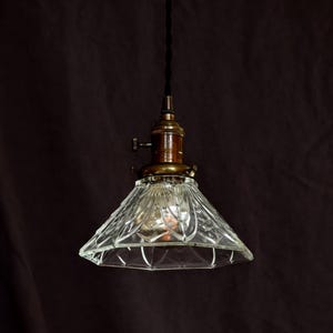 Op de afbeelding: Een hanglamp van helder glas met een messing afwerking en een ruitvormig patroon. De lamp hangt aan een zwart snoer.