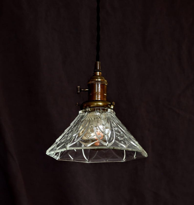Op de afbeelding: Een hanglamp van helder glas met een messing afwerking en een ruitvormig patroon. De lamp hangt aan een zwart snoer.