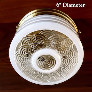May include: A white ceiling light fixture with a brass trim and a decorative glass shade. The shade has a pattern of overlapping circles and is 6 inches in diameter.