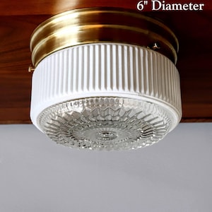 May include: A 6-inch diameter ceiling light fixture with a white ribbed glass shade and a clear glass diffuser. The fixture has a brass finish.