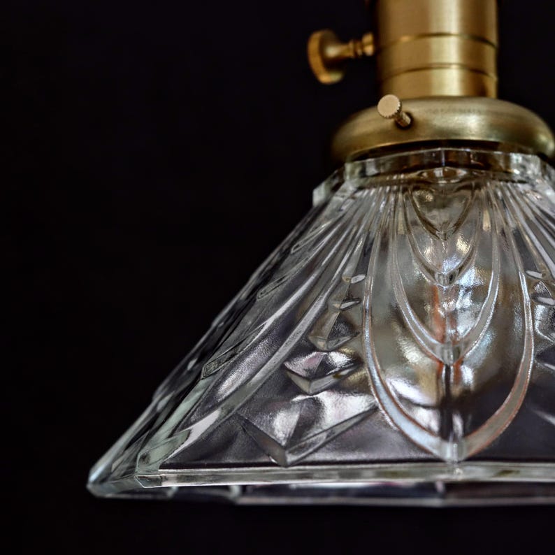 Op de afbeelding: Een transparante glazen lampenkap met een geometrisch patroon. De lampenkap is bevestigd aan een messing lampfitting met een knop.