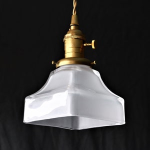 Op de afbeelding: Een messing hanglamp met een vierkante kap van matglas. De kap heeft een licht afgeronde boven- en onderkant.