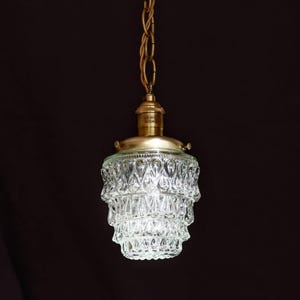 May include: A brass pendant light with a clear glass shade featuring a tiered, faceted design. The shade is made of many small, diamond-shaped pieces.