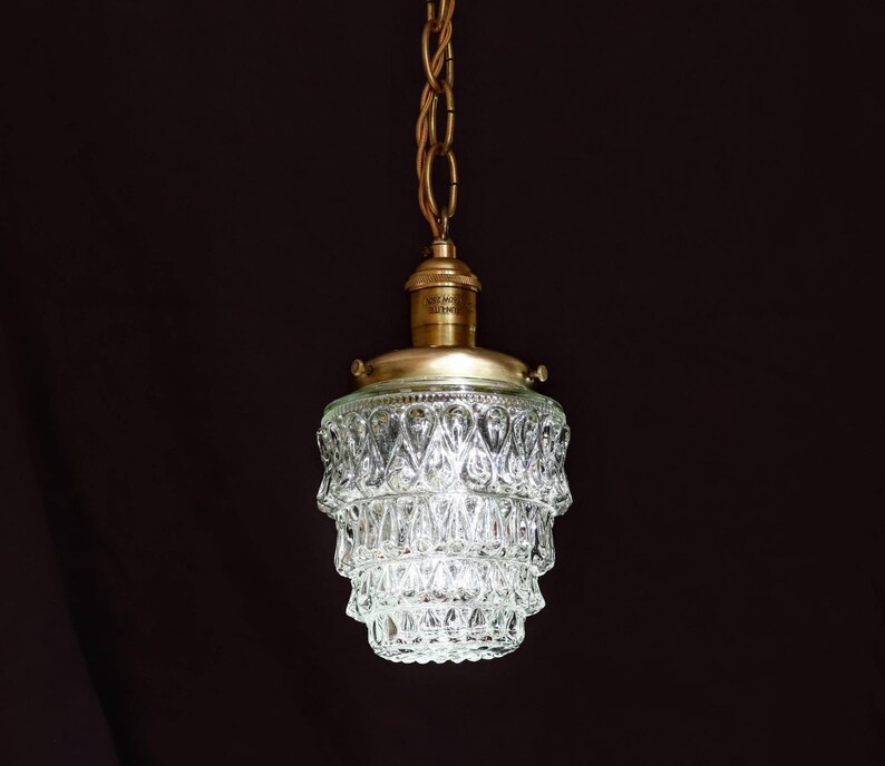 May include: A brass pendant light with a clear glass shade featuring a tiered, faceted design. The shade is made of many small, diamond-shaped pieces.