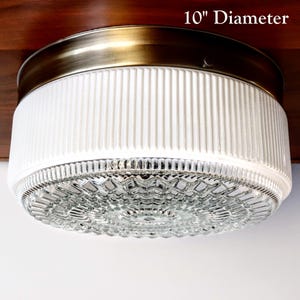 May include: A white ceiling light fixture with a brass trim and a clear glass diffuser. The light is 10 inches in diameter.
