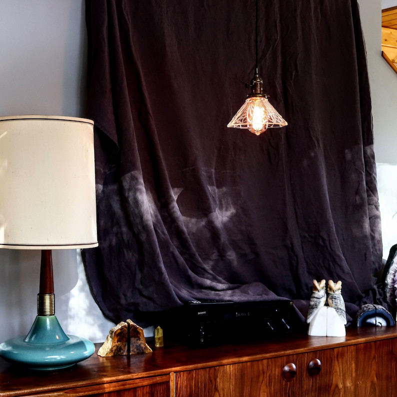 Op de afbeelding: Een vintage-stijl tafellamp met een witte kap en een tealblauwe basis. De lamp staat op een houten tafel met een zwarte stereo-ontvanger en twee uil-boekenleggers.