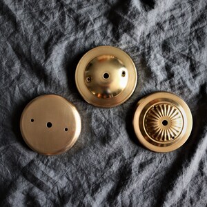 Op de afbeelding: Drie goudkleurige metalen plafondlamp-afdekkingen. De afdekkingen zijn rond en hebben verschillende ontwerpen. E&eacute;n afdekking heeft een glad oppervlak, een andere heeft een reli&euml;fpatroon en de derde heeft een klein gaatje in het midden.