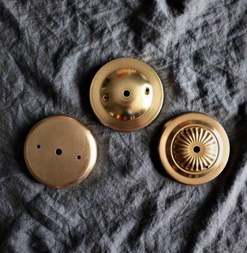 Op de afbeelding: Drie goudkleurige metalen plafondlamp-afdekkingen. De afdekkingen zijn rond en hebben verschillende ontwerpen. E&eacute;n afdekking heeft een glad oppervlak, een andere heeft een reli&euml;fpatroon en de derde heeft een klein gaatje in het midden.