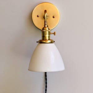 May include: A brass wall sconce with a white, textured glass shade. The sconce has a simple design and a classic look.