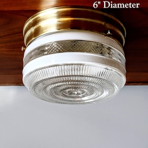 May include: A 6-inch diameter ceiling light fixture with a brass trim and a white glass shade. The glass shade has a clear, textured pattern.