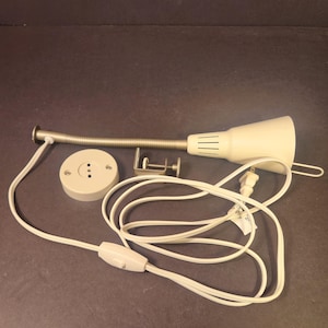 May include: A cream-colored desk lamp with a flexible metal neck and a clamp. The lamp has a white cord with an on/off switch and a plug. Also included is a white base with three holes and a metal clamp.