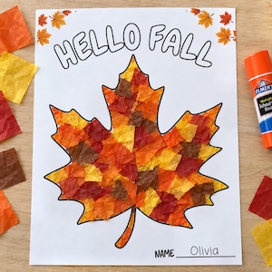 May include: A white paper craft sheet featuring the text HELLO FALL at the top and a large maple leaf outline filled with small, crinkled squares of orange, yellow, red, and brown tissue paper. The name Olivia is written on the bottom line.