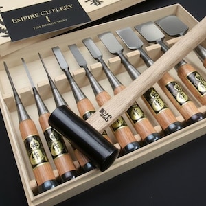 May include: A set of Empire Cutlery Japanese wood carving tools in a wooden box. The set includes various chisels, gouges, and a wooden mallet. The tools have wooden handles with metal blades and are arranged neatly inside the box.