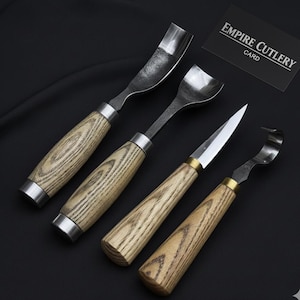 May include: A set of four wood carving tools with metal blades and wooden handles. The handles have a light wood grain pattern. The blades are various shapes, including curved and pointed. The Empire Cutlery card is in the background.
