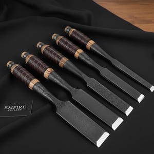 May include: A set of five chisels with dark metal blades and wooden handles wrapped in brown leather. The chisels are arranged diagonally on a black surface. The brand name "EMPIRE CUTLERY" is visible on a small card.