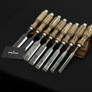 May include: A set of eight wood chisels with silver blades and wooden handles, displayed in a brown leather tool roll. The chisels are arranged in a row, with the blades facing forward. A business card with the text "EMPIRE CUTLERY" is in the foreground.