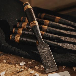 May include: A set of wood chisels with dark wooden handles and textured metal blades. The handles feature a combination of dark wood, light wood, and black leather-like bands. The blades have a hammered texture. The Empire Cutlery logo is visible.