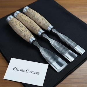 May include: Four wood carving chisels with wooden handles and metal blades are displayed on a black surface. The handles have a light wood grain pattern and are capped with silver metal. A white card with "Empire Cutlery" is in the foreground.