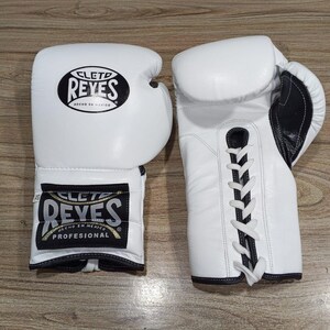 Peut inclure: Paire de gants de boxe en cuir blanc avec des détails noirs. Les gants portent le logo "CLETO REYES" en noir et le texte "HECHO EN MEXICO". Les gants sont lacés à l'arrière.