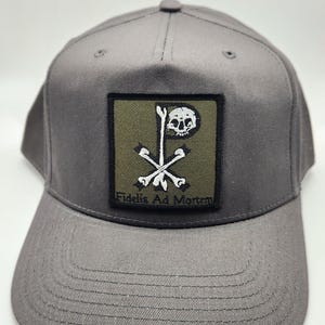 May include: Gray baseball cap with a structured brim and a square patch. The patch features a skull and crossbones design with the text "Fidelis Ad Mortem" in white. The cap is made of a durable fabric.