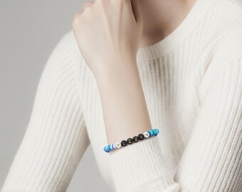 Puede incluir: Una pulsera de cuentas con el nombre "LIZZY" escrito con cuentas de letras negras y blancas. La pulsera presenta cuentas azules, blancas y doradas. La pulsera se lleva en la muñeca.